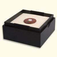 Jasper Mourning Button lies in the open box on the red side of the reversible cushion. The other side is light yellow. LxW = ± 125x125mm.