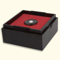 Onyx Mourning Button lies in the open box on the red side of the reversible cushion. The other side is light yellow. LxW = about 125x125mm.